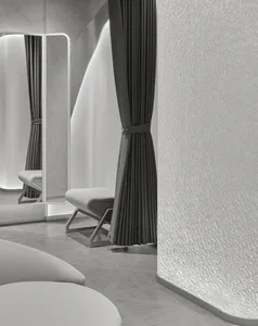 Modern minimalist dressing room featuring curved textured plaster walls, dark grey pleated curtains, white leather bench, and a tall backlit mirror with LED lighting.