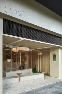 Modern minimalist coffee shop exterior with concrete facade, large glass windows, wooden signage, and hanging pendant lights.