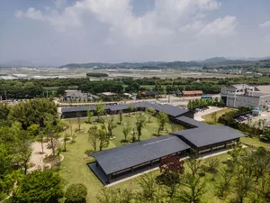 Aerial photograph of a modern cultural center in Yilan, Taiwan, featuring long dark-roofed buildings arranged in an L-shape, surrounded by green lawns, trees, and rural landscape with mountains in the background.