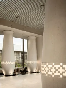 Modern minimalist lobby with three large sculptural concrete columns featuring illuminated geometric tile bands, curved ribbed ceiling, and polished terrazzo floor.