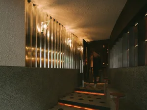Modern entrance hallway featuring a ribbed brushed brass wall, integrated wall sconces, textured concrete surfaces, and a staircase with glowing orange LED riser lighting.