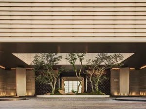 Modern luxury hotel lobby entrance with indoor zen garden, mature trees, travertine floors and linear ceiling lighting