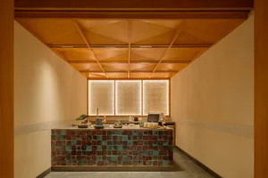 Modern Japanese-style tea room with a long counter covered in multicolored iridescent ceramic tiles, wooden geometric ceiling, and backlit textured glass windows.