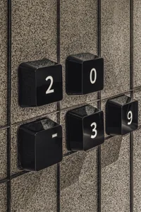Close-up of modern black cube-shaped apartment unit signage with white numbers mounted on a grey terrazzo tiled wall.