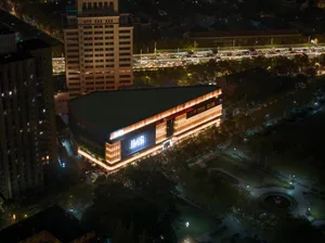 Aerial night view of a modern rectangular commercial building with dramatic orange linear facade lighting, surrounded by trees and city traffic in Taipei.