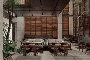Spacious modern restaurant interior featuring exposed concrete walls, wooden slat screens, built-in seating, wooden dining tables, and abundant indoor trees under a high ceiling.