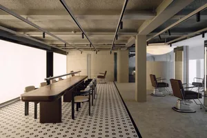 Modern brutalist hair salon interior featuring a long walnut styling counter, cream upholstered chairs, brown leather salon chairs on chrome bases, black and white patterned terrazzo floor, and raw concrete ceiling with linear lighting.