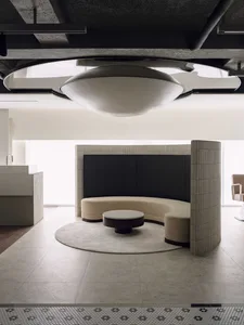 Modern minimalist lounge featuring a large curved beige boucle sofa, round dark coffee table on a circular rug, dramatic circular ceiling light fixture, micro-cement floors and textured concrete walls.