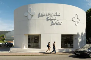 Modern cylindrical white pharmacy building with curved facade, large flower and cross signage, and glass storefront under bright daylight.