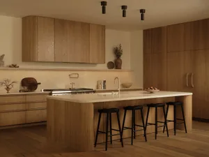 Modern minimalist kitchen featuring light oak cabinetry, a large white quartz kitchen island with black stools, and warm ambient lighting.
