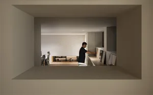 View into a minimalist home office with built-in oak cabinetry, a man arranging artwork, and an ergonomic chair at a desk.