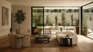 Modern living room with cream linen sofa, armchair, dark wood coffee table, large potted fiddle leaf fig, and open view to a stone-walled outdoor courtyard with dining area.