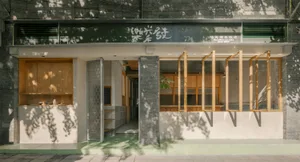 Street view of Shanwei Lei Cha Rice Shop featuring a modern facade with light wood cabinetry, grey concrete pillars, green painted base, and large openable wooden windows under a dark green signboard.