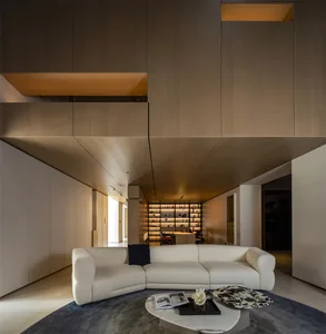 Modern minimalist living room featuring a large curved white sectional sofa, dramatic wooden ceiling panels with hidden lighting, marble coffee table, and a built-in illuminated display wall in the background.