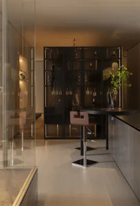 Modern luxury home bar with black oak illuminated wine cabinet, brown leather bar stool, and round black table in a warm ambient setting.