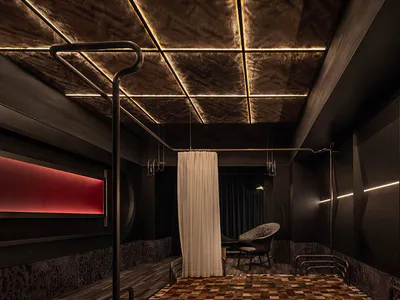 Dark luxury bedroom featuring a black metal four-poster bed, patchwork cowhide leather floor, textured dark walls, and dramatic linear ceiling lighting.