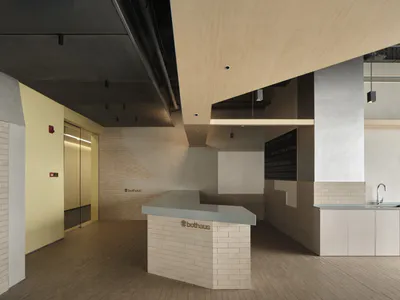 Modern minimalist reception desk made of white brick with a light gray countertop, set in an open commercial interior with birch wood ceiling elements and concrete walls.