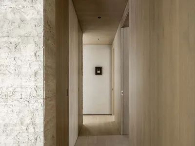 狹長極簡風走廊，左側為質感白色洞石牆面，搭配淺色橡木木板牆與天花板，以及淺色木地板。