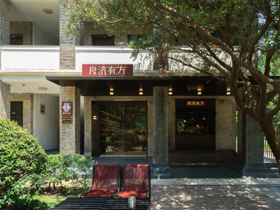 兩層樓清水磚歷史建築外觀，招牌寫有「良濟有方」，設有現代玻璃入口、木棧板、兩張紅色躺椅與大樹遮蔭。