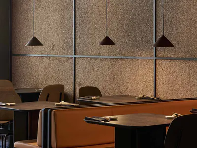 Modern Japanese-style restaurant interior with brown cork tile walls, burnt orange leather booth seating, dark wood tables, and pendant lights over a patterned blue and brown carpet.