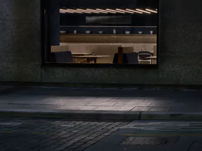 Night view through a large window into a minimalist Japanese restaurant interior featuring a terrazzo counter, wooden dining benches, and linear pendant lighting.