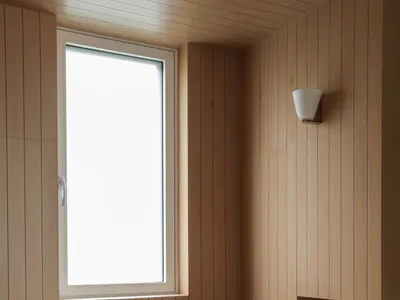 Modern minimalist bathroom featuring a built-in corner wooden bathtub, light oak vertical wall paneling, a large window, and a chrome wall-mounted faucet.