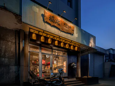 夜晚的福丸燒肉酒場日式居酒屋，波浪鐵皮外牆、發光的紙燈籠、復古木招牌，前方停著一輛黑色重型機車。