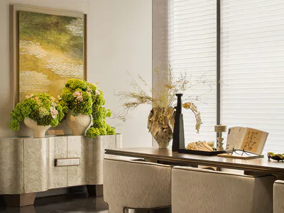 Modern minimalist dining room featuring a textured beige sideboard with large green hydrangea arrangements, a wooden dining table with sculptural dried floral centerpiece, beige upholstered dining chairs, and a large abstract landscape painting on the wall.