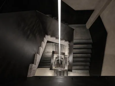 Looking down into a dramatic concrete spiral staircase with a powerful vertical linear light fixture descending through the center of the void.