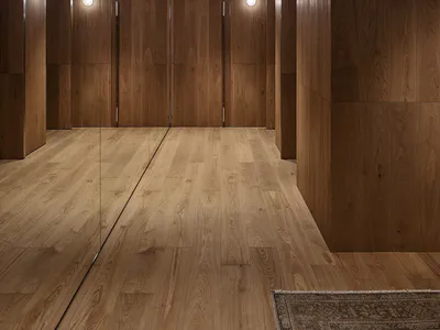 Modern walk-in closet interior featuring rich walnut wood paneling, full-height mirrored closet doors, recessed ceiling lights, and warm wall sconces.