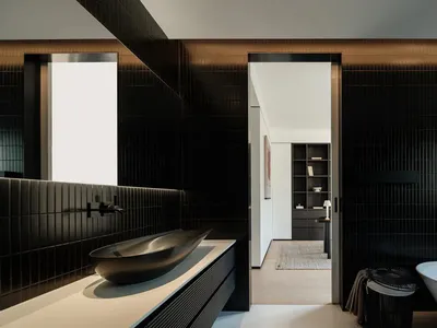 Modern luxury bathroom with black ribbed tiles, a freestanding white bathtub, bronze vessel sink on a white countertop, and a view into a walk-in closet.