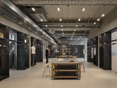 現代工業風服裝精品店室內，裸露混凝土牆面、黑色金屬層架、中央木質展示桌與軌道燈光。