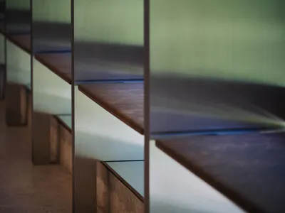 Close-up view of a minimalist concrete staircase with floating brushed metal shelves in soft diffused lighting.