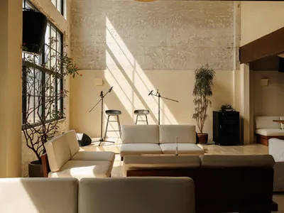 Modern industrial-style lounge with white modular sofas, draped fabric ceiling, exposed concrete walls, and dramatic natural light patterns.