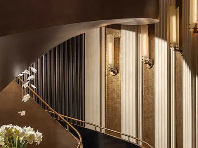 Elegant curved grand staircase with illuminated steps, polished brass handrails, dark reflective balustrades, and large white orchid and hydrangea floral arrangements in a luxurious interior space.