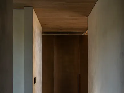Narrow minimalist hallway featuring concrete walls, dark wood cabinetry, wood plank ceiling, and dark tiled floor.