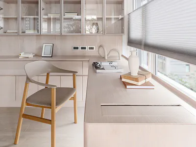 Modern minimalist home office with light wood built-in cabinetry, a wooden chair with upholstered seat, large windows with blinds, and decorative objects on the desk.