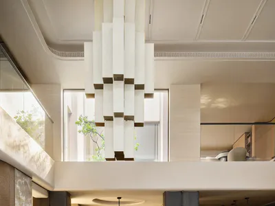 Modern luxury dining room featuring a large round dark marble table with ten cream upholstered chairs, dramatic geometric white chandelier, double-height ceiling, and views to upper level and wine cellar.