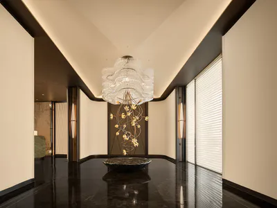 Modern luxury hotel lobby featuring a large sculptural crystal chandelier with cascading golden floral elements, dark polished marble floor, and recessed ceiling lighting.