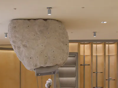Modern mineral gallery reception desk with a massive floating raw stone boulder installation and illuminated display cases in the background.