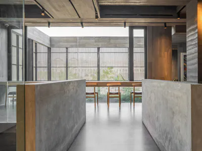 現代極簡用餐區，設有大型清水混凝土隔板、木製餐椅、長木桌，以及可眺望綠意的大型垂直格柵窗戶。