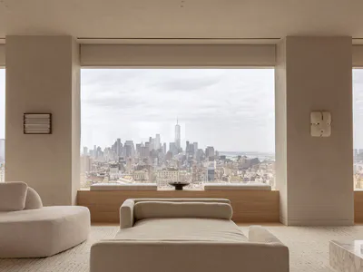 現代極簡客廳，前景為大型泡泡紗布料躺椅與 chaise，透過落地窗可見包含世界貿易中心一號樓的紐約市天際線。