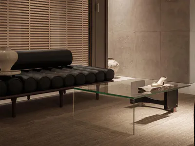 Modern minimalist living room featuring a black leather cylindrical daybed, glass coffee table, textured concrete walls, and wooden blinds with warm ambient lighting.