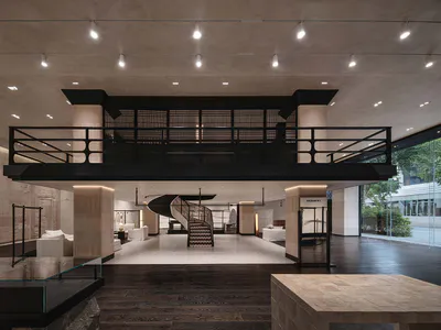 Interior view of a luxury fashion boutique with a dramatic double-height ceiling, black metal railing on the mezzanine, a sculptural spiral staircase in the center, travertine stone walls and floors, and minimalist white seating areas.