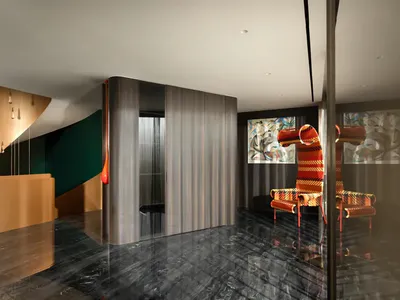 Modern luxury hotel lobby with curved metallic reception desk, dark polished marble floor, hanging pendant lights, and colorful patterned armchairs against abstract art.