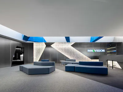 Modern corporate lobby interior with blue modular sofas, geometric lighting features, and a large illuminated INNOVISION logo on a dark wall with circuit board patterns.