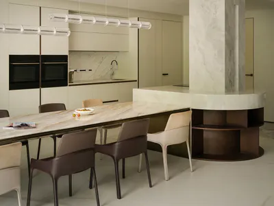 Modern minimalist dining room featuring a large curved marble kitchen island, a long marble dining table with mixed-tone dining chairs, pendant lights, and a sculptural curved ceiling detail.