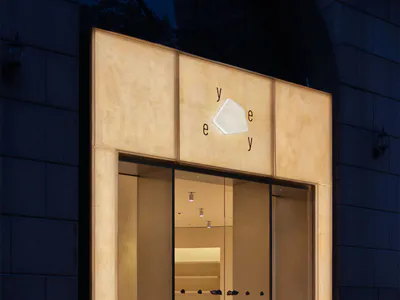 夜間現代極簡店面，外牆使用大面積背光洞石板材，大面積玻璃入口，品牌名稱 Yeye 清晰呈現於立面與階梯上。