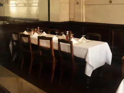 Interior view of a traditional British-style restaurant dining room featuring a long white-clothed table, dark wood chairs, and walls decorated with framed cricket memorabilia including signed jerseys.