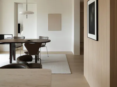 Modern minimalist dining room featuring a dark oak oval table, brown leather chairs, a large white pendant lamp, light oak wall paneling, and a neutral area rug.